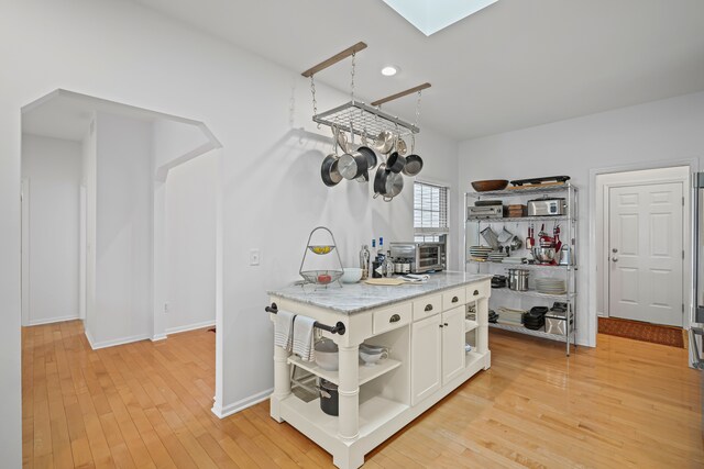 kitchen with a skylight, open shelves, white cabinetry, light stone counters, and light wood-style flooring