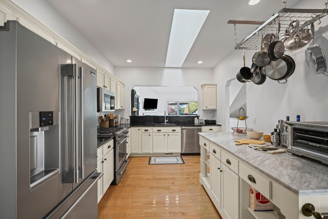 kitchen with high end appliances, light wood-type flooring, a sink, a toaster, and recessed lighting
