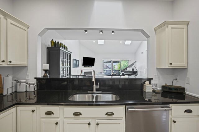 kitchen featuring dark countertops, arched walkways, stainless steel dishwasher, a sink, and open floor plan