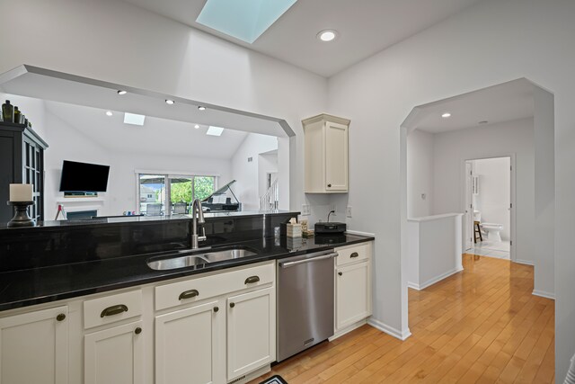 kitchen with dark countertops, a sink, light wood-type flooring, stainless steel dishwasher, and a skylight