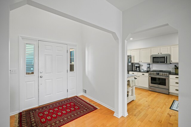 entrance foyer featuring baseboards, visible vents, a high ceiling, and light wood-style floors