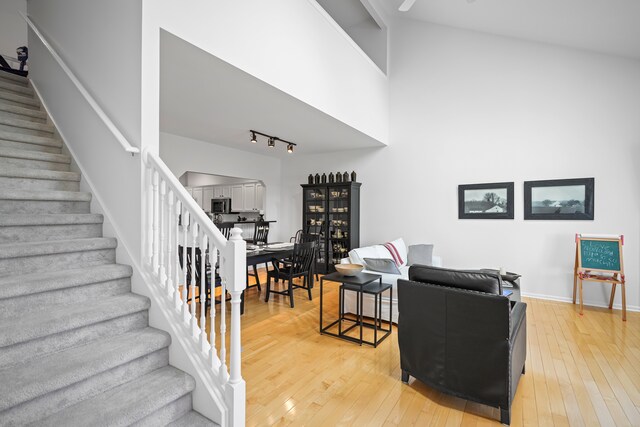 living area featuring baseboards, light wood-style flooring, stairs, and a towering ceiling