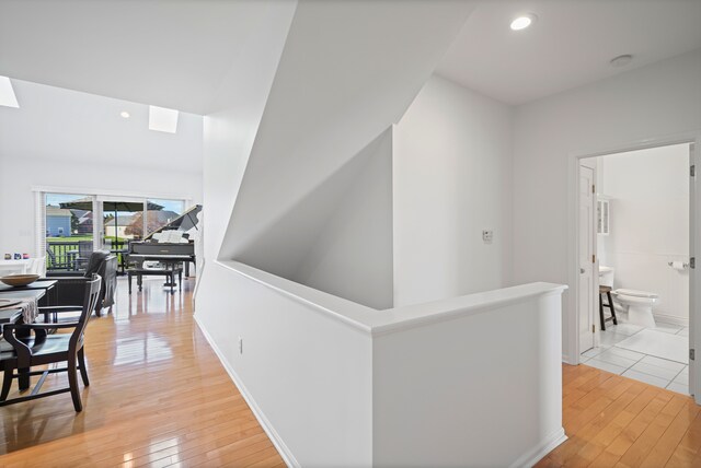 hall with recessed lighting, a skylight, light wood finished floors, and an upstairs landing