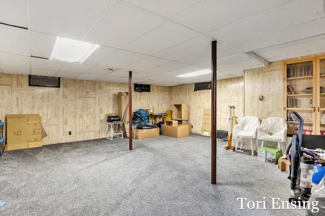finished basement with carpet floors, wood walls, and a drop ceiling