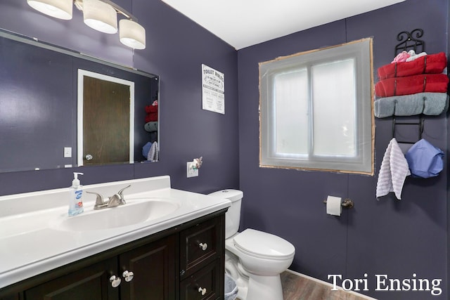 half bathroom featuring toilet, wood finished floors, and vanity