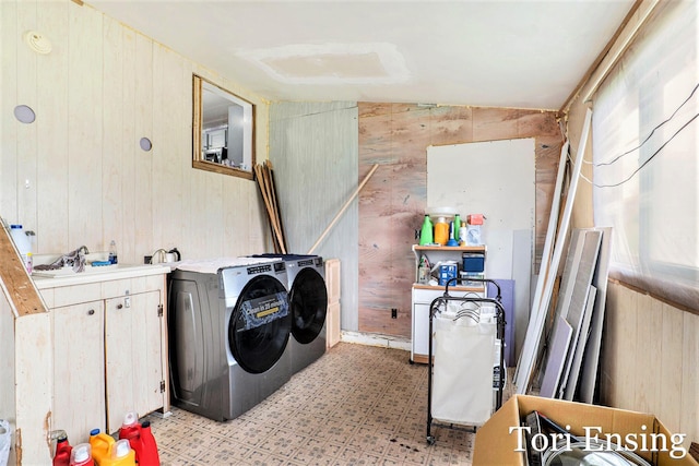 clothes washing area featuring washer and dryer, light floors, wooden walls, a sink, and cabinet space