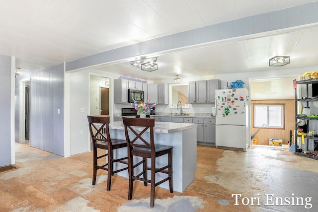 kitchen featuring freestanding refrigerator, a breakfast bar area, electric stove, a sink, and gray cabinetry