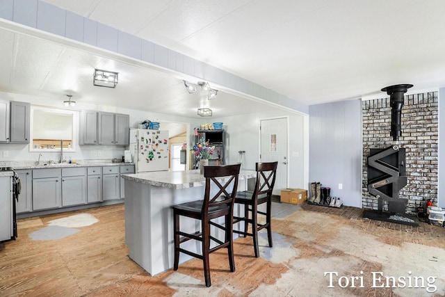 kitchen featuring freestanding refrigerator, a breakfast bar area, light countertops, gray cabinets, and a sink