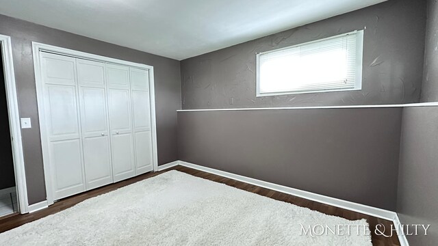 unfurnished bedroom with dark wood-style flooring, baseboards, and a closet