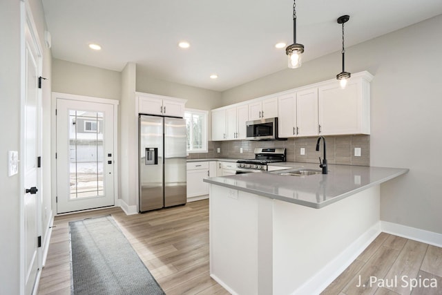 kitchen featuring decorative backsplash, appliances with stainless steel finishes, a sink, a peninsula, and light wood finished floors