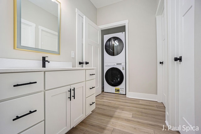 laundry area featuring light wood-style floors, baseboards, a sink, cabinet space, and stacked washer / drying machine