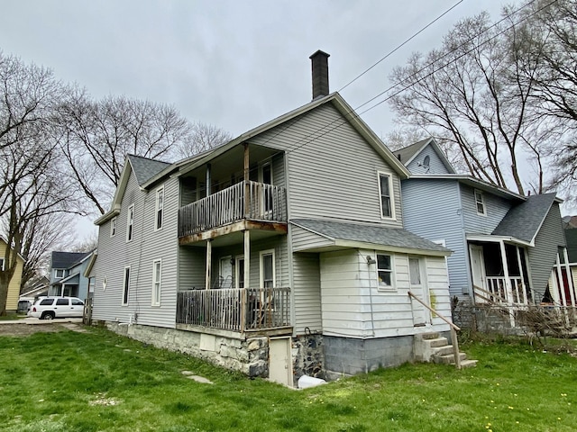 rear view of house with roof with shingles, a yard, a balcony, and a chimney