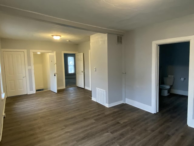 empty room with visible vents, baseboards, and dark wood finished floors