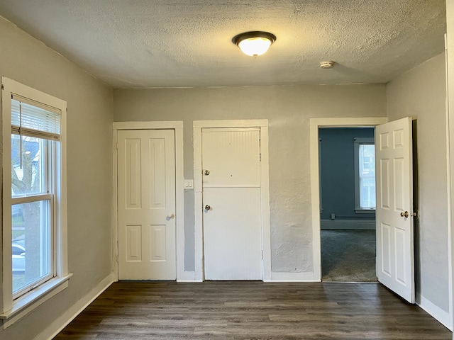 unfurnished bedroom with baseboards, a textured ceiling, and dark wood finished floors