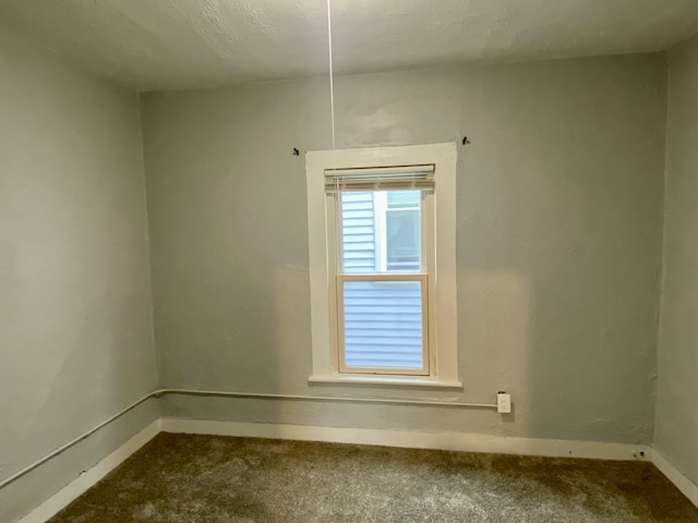 spare room with baseboards and dark carpet