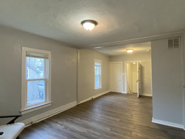 empty room featuring baseboards, dark wood-type flooring, a textured ceiling, and visible vents
