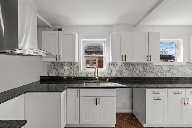 kitchen with wall chimney range hood, tasteful backsplash, a sink, and visible vents