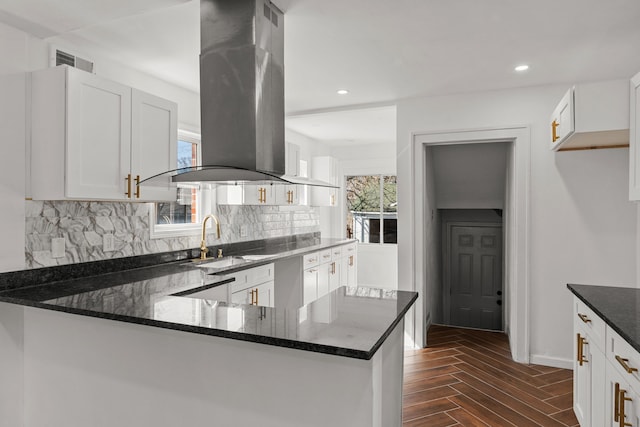 kitchen with decorative backsplash, visible vents, island range hood, a sink, and dark stone counters