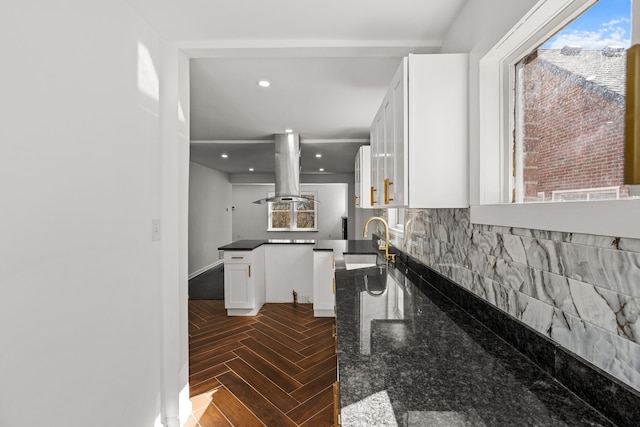 kitchen with a healthy amount of sunlight, backsplash, island exhaust hood, a sink, and white cabinetry