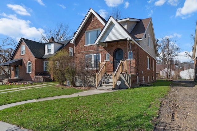 view of front facade featuring roof with shingles, a front yard, and brick siding