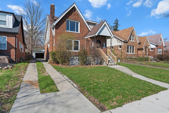 tudor house with brick siding, a chimney, a front yard, and concrete driveway