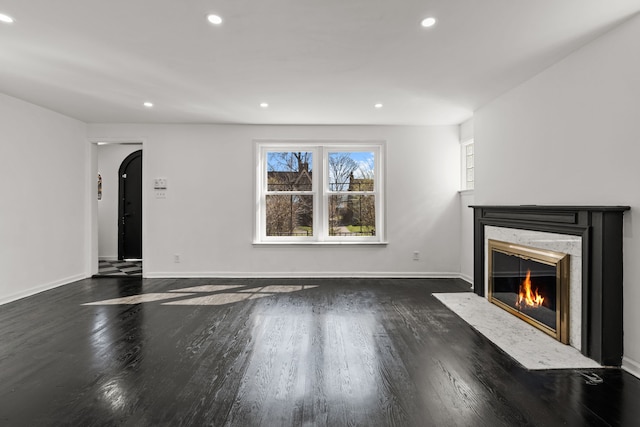 unfurnished living room with arched walkways, recessed lighting, wood finished floors, and a premium fireplace