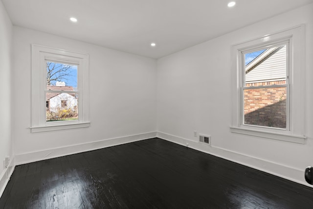 empty room featuring a healthy amount of sunlight, baseboards, dark wood-type flooring, and visible vents
