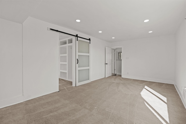 unfurnished bedroom with recessed lighting, a barn door, and light carpet
