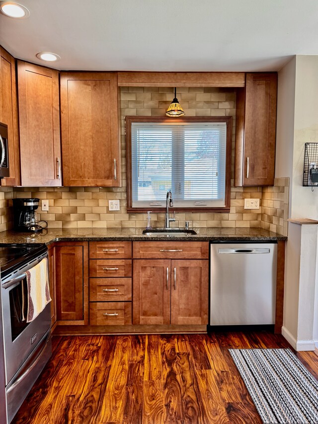 kitchen featuring brown cabinets, appliances with stainless steel finishes, a sink, dark stone countertops, and tasteful backsplash