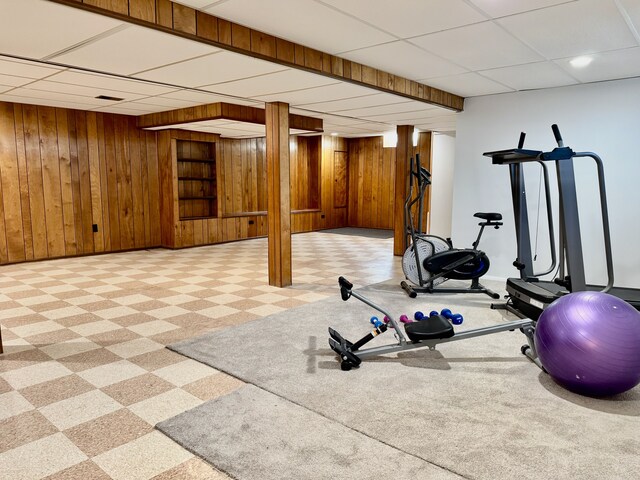 workout room featuring tile patterned floors, wood walls, a drop ceiling, and baseboards