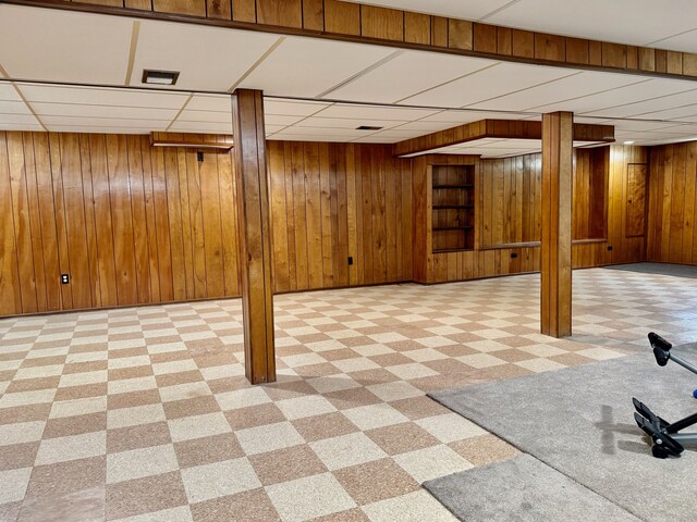 finished below grade area with wood walls, a drop ceiling, and tile patterned floors