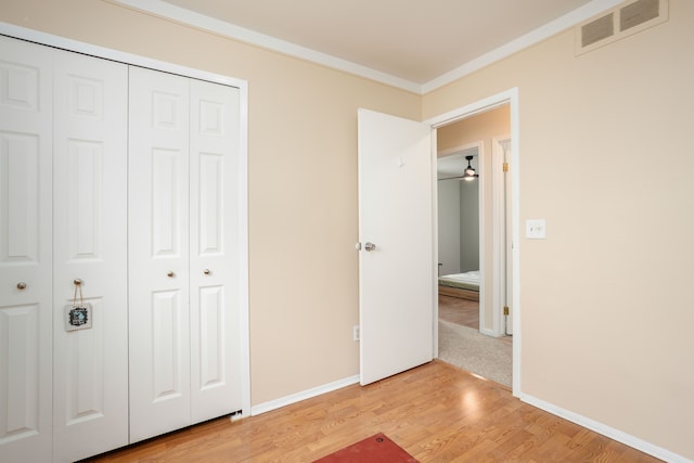 unfurnished bedroom with light wood-style floors, baseboards, visible vents, ornamental molding, and a closet