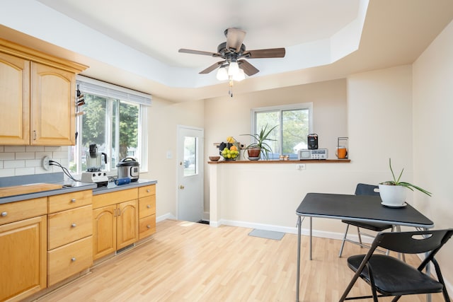 kitchen with a ceiling fan, light wood finished floors, a tray ceiling, and light brown cabinets