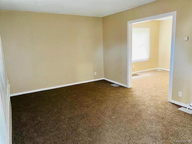 empty room with baseboards, dark carpet, and visible vents