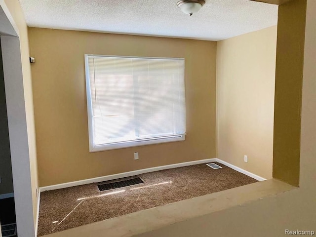 carpeted empty room with a textured ceiling, baseboards, and visible vents