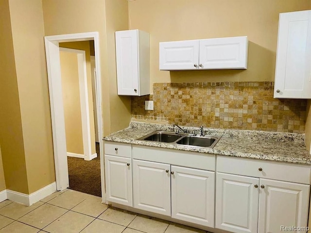 kitchen with a sink, backsplash, baseboards, and white cabinets