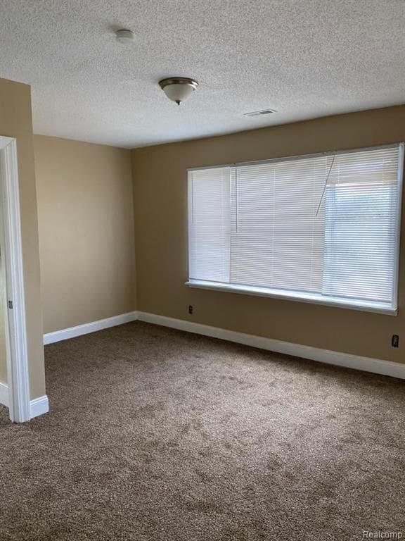carpeted spare room featuring plenty of natural light, visible vents, baseboards, and a textured ceiling