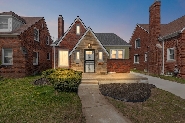 tudor home with a lawn, a chimney, and brick siding