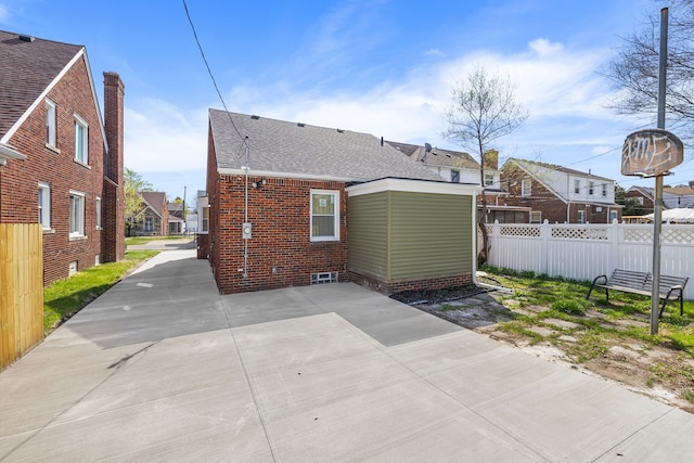 back of house featuring brick siding, roof with shingles, fence, and a residential view