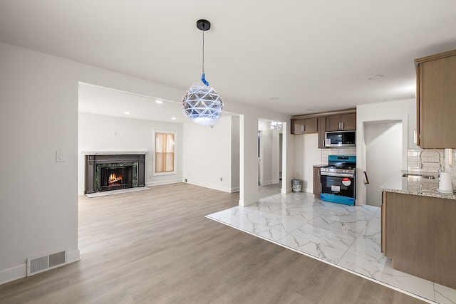 unfurnished living room with visible vents, baseboards, a warm lit fireplace, recessed lighting, and a sink