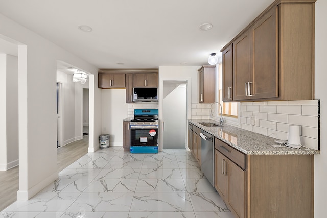 kitchen featuring appliances with stainless steel finishes, light stone countertops, a sink, baseboards, and marble finish floor