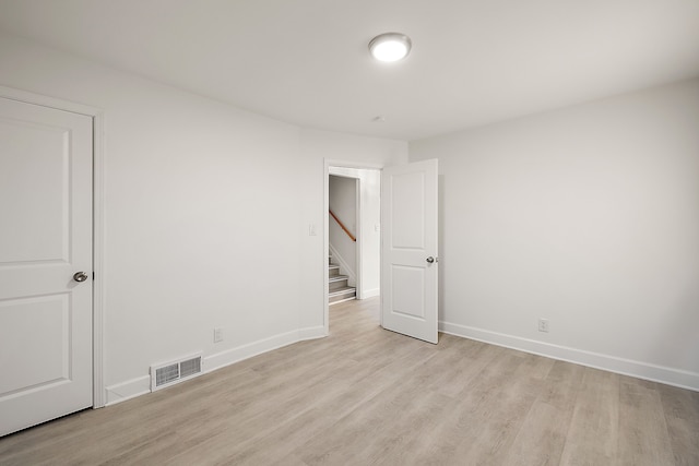 spare room featuring light wood-style floors, baseboards, stairs, and visible vents