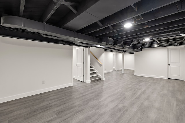 finished basement with baseboards, wood finished floors, and stairway