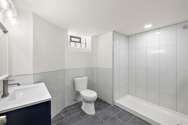 full bathroom with a tile shower, vanity, toilet, tile patterned floors, and tile walls