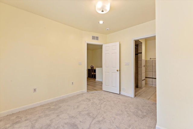 unfurnished bedroom featuring baseboards, ensuite bathroom, carpet flooring, and visible vents