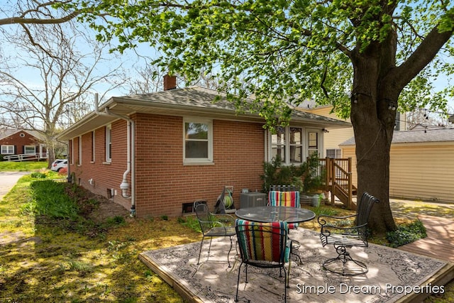 rear view of house with a chimney, brick siding, a patio, a shingled roof, and outdoor dining space