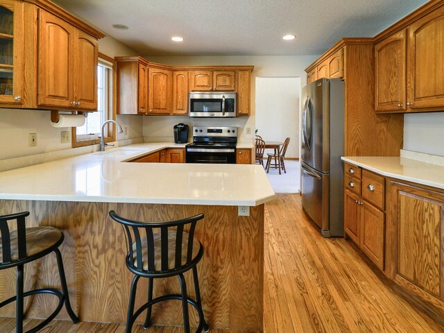 kitchen with brown cabinets, appliances with stainless steel finishes, a sink, light wood-style flooring, and a peninsula