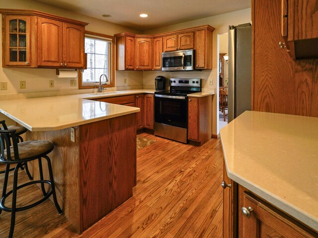 kitchen with a peninsula, a kitchen breakfast bar, light wood-type flooring, a sink, and appliances with stainless steel finishes