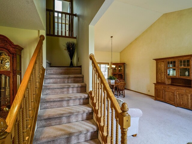 stairs with carpet flooring, high vaulted ceiling, an inviting chandelier, and baseboards