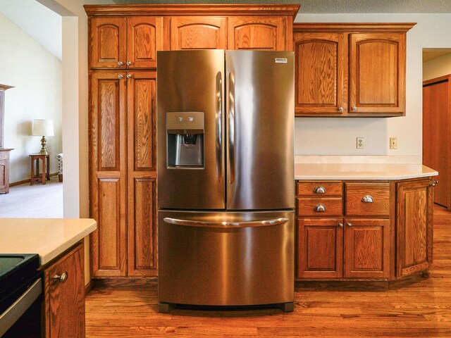 kitchen featuring stainless steel fridge, light countertops, brown cabinetry, and dark wood-style floors
